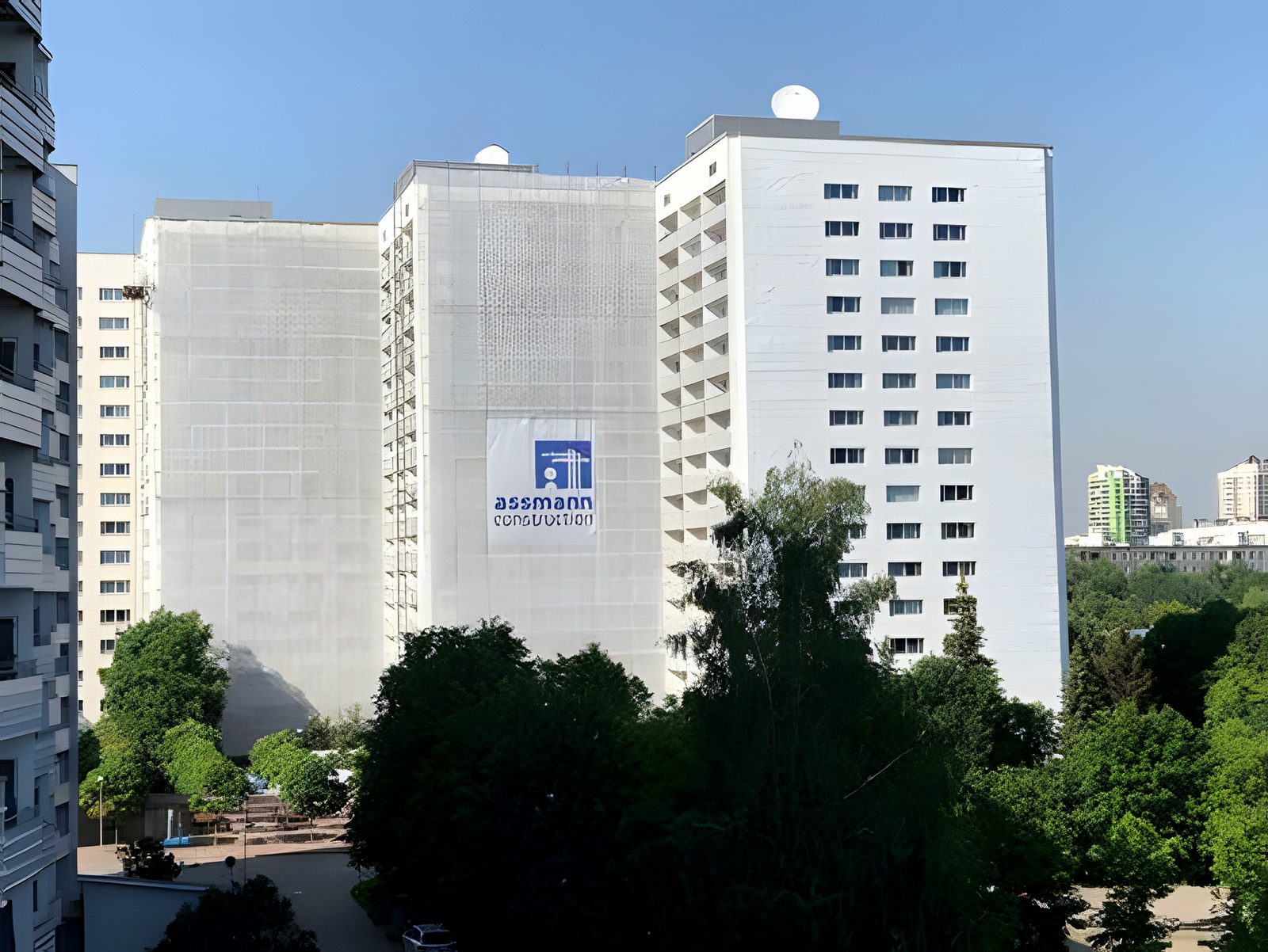 Refurbished white residential slab blocks behind summer trees