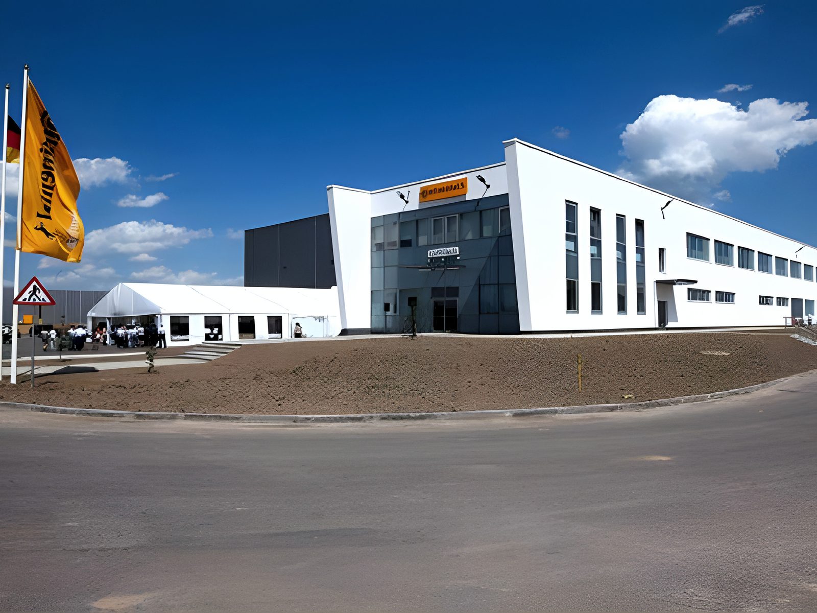 White plant building and flagpoles seen from the access road