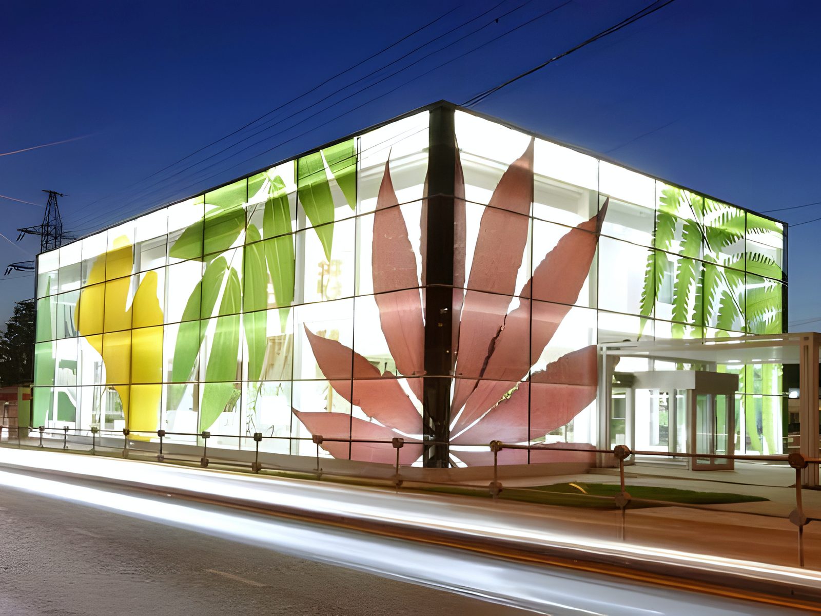 Night exterior of glass sales pavilion with leaf-printed facade