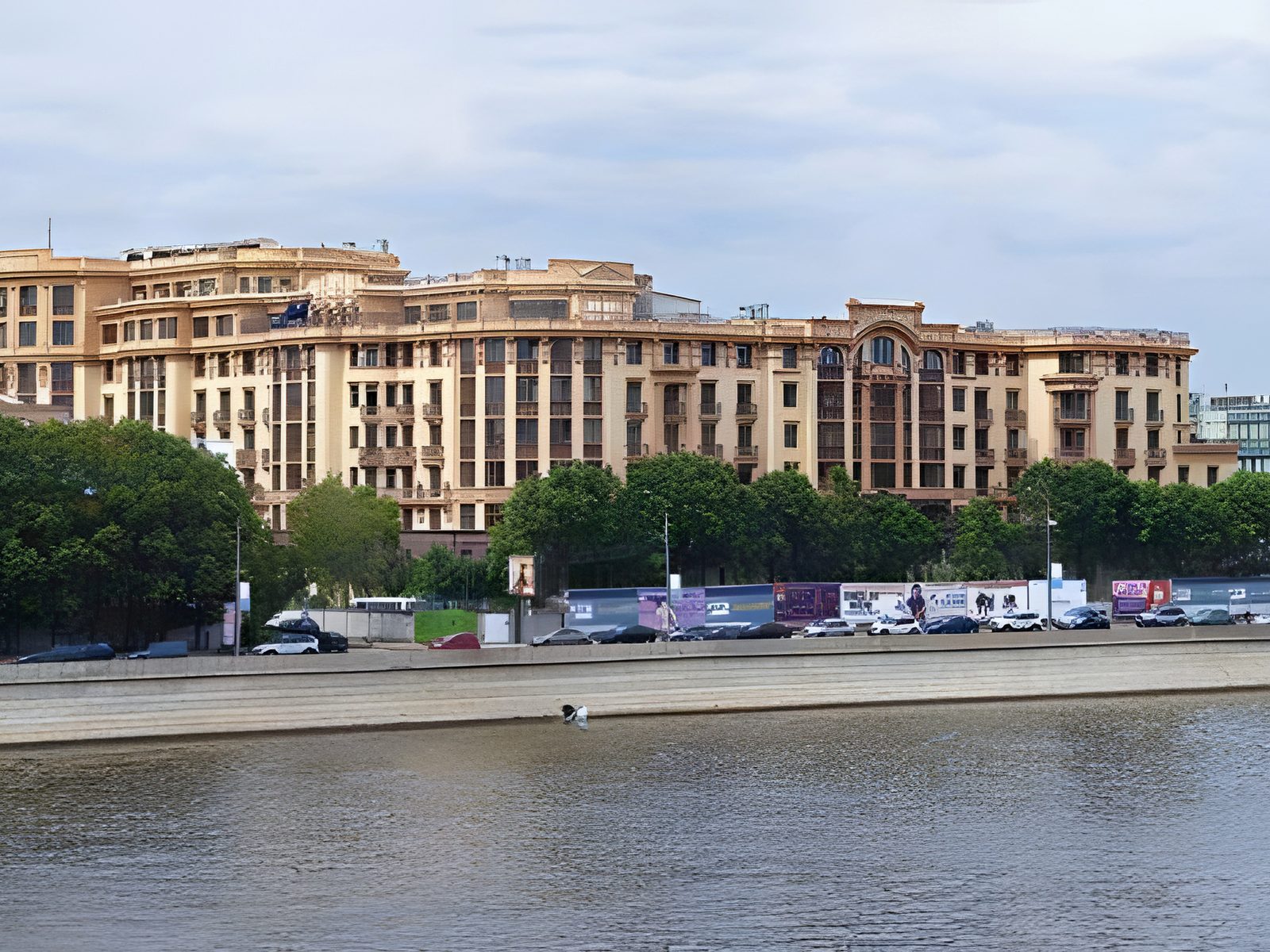 Classical-style complex along a river embankment behind trees