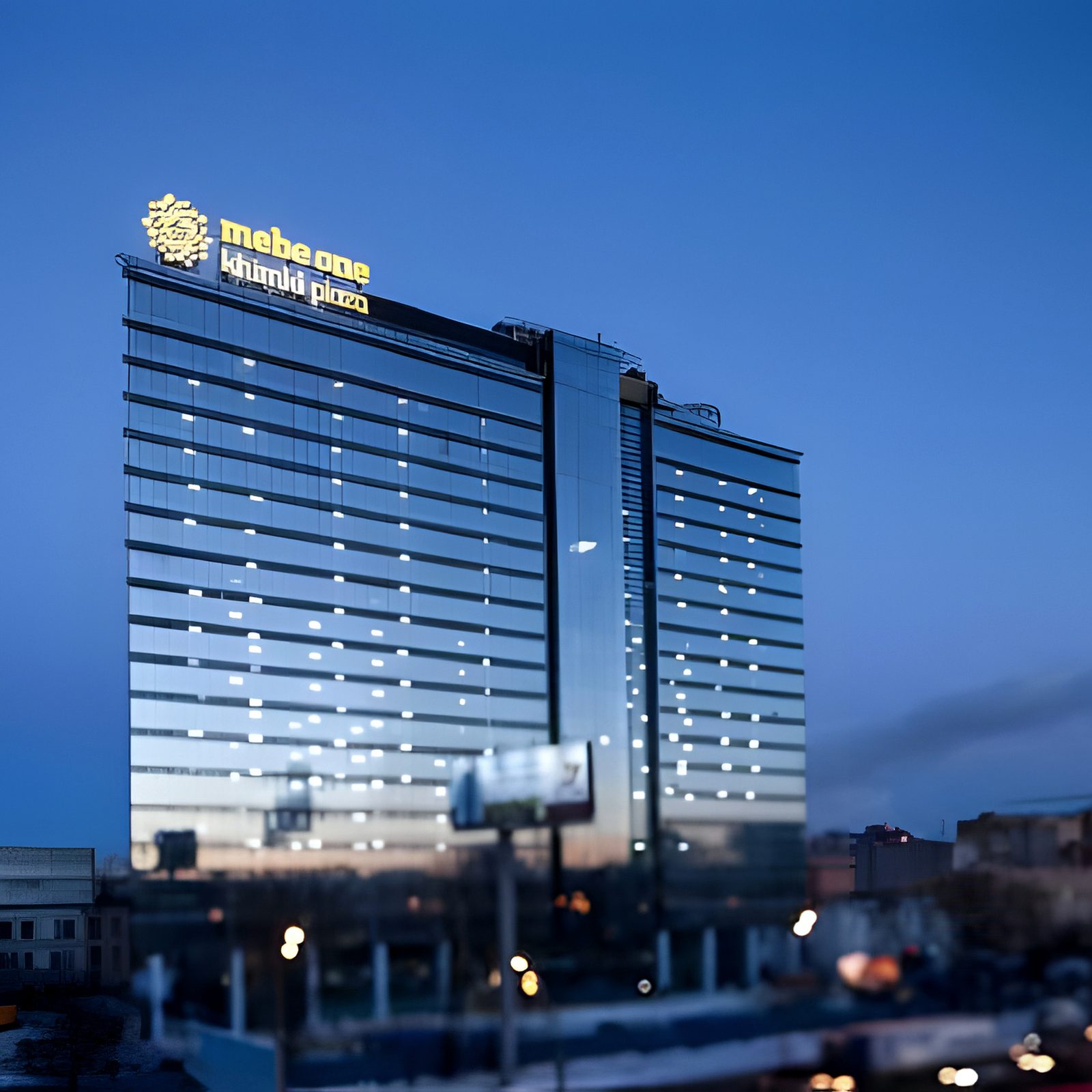 Blue-hour office tower with lit roof sign above city lights