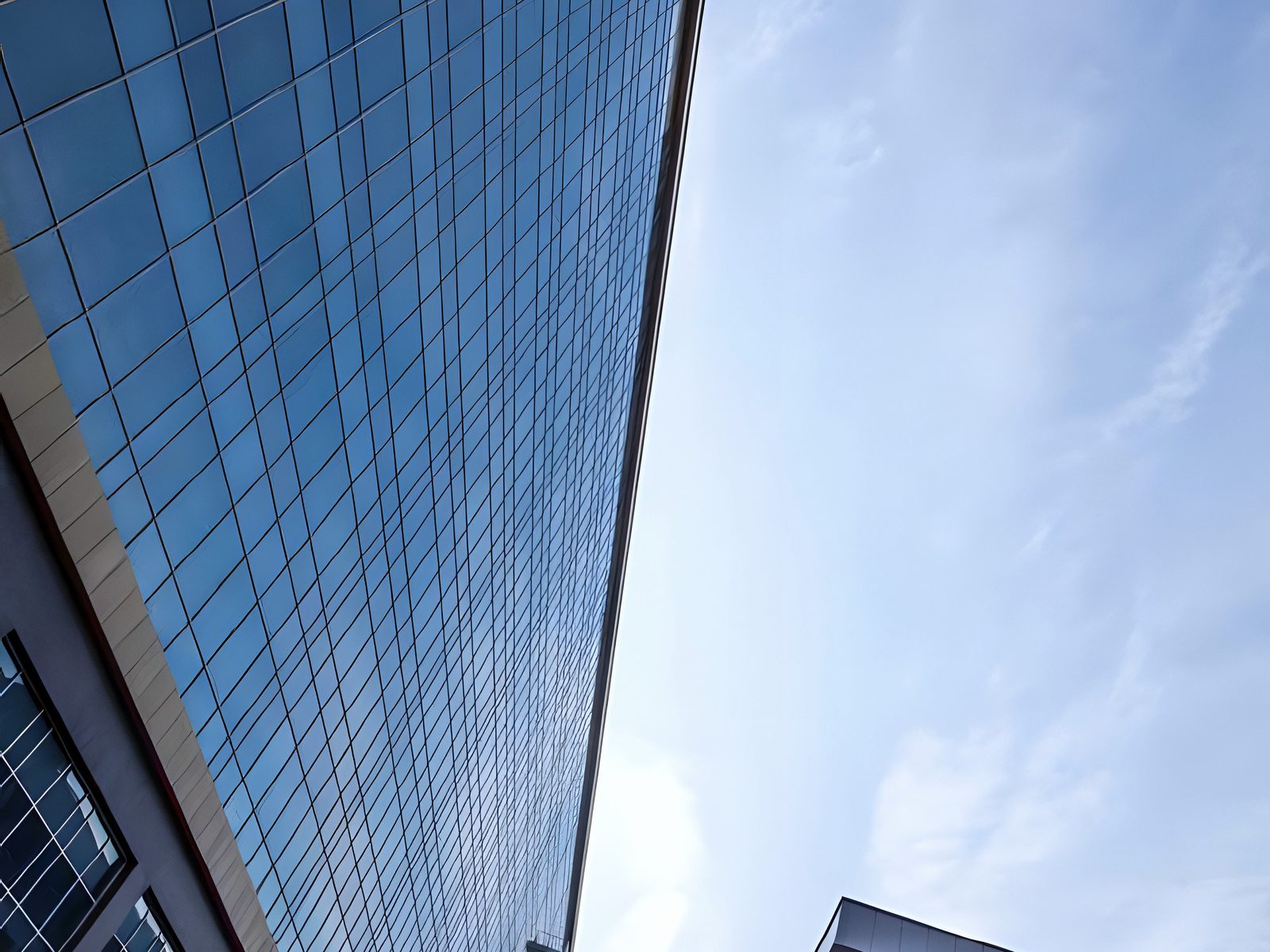 Steep upward view along tinted glass curtain wall against sky