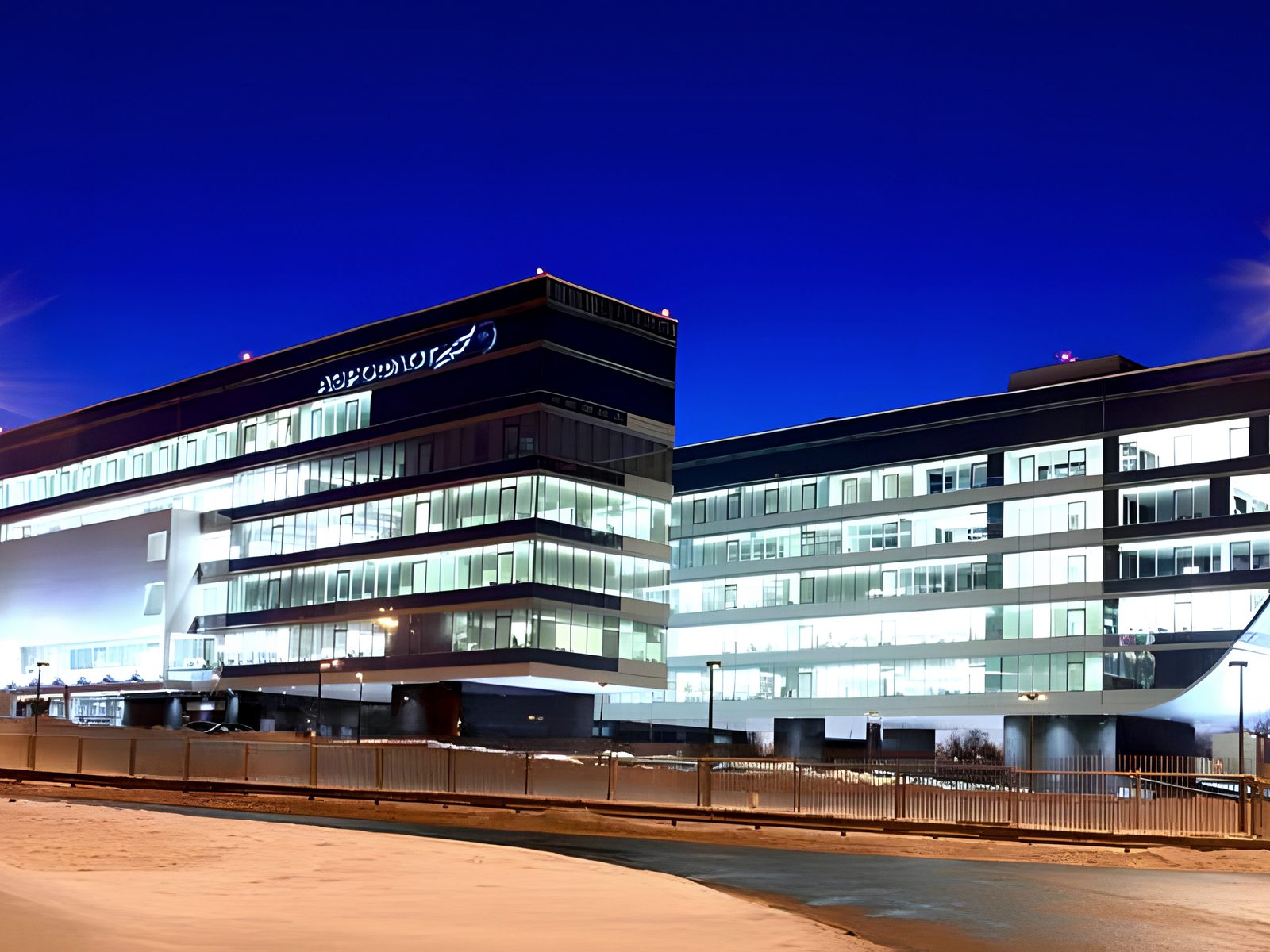 Blue-hour view of lit winged glass headquarters from the road