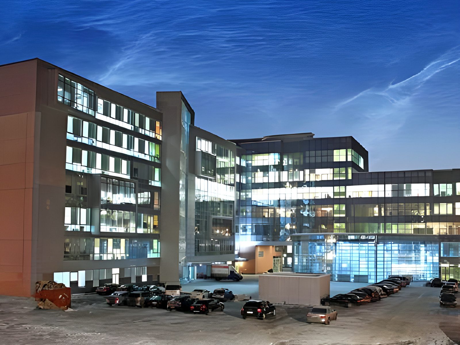 Brick-and-glass office block at dusk, cars parked outside