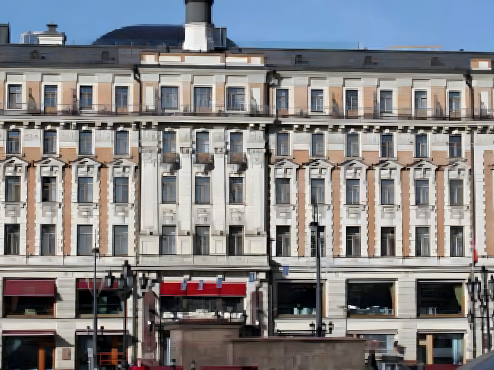 Neo-classical hotel block on a Moscow street: rusticated stone base with dark-red awnings over shop windows, orange-and-white pilastered upper floors, mansard roof