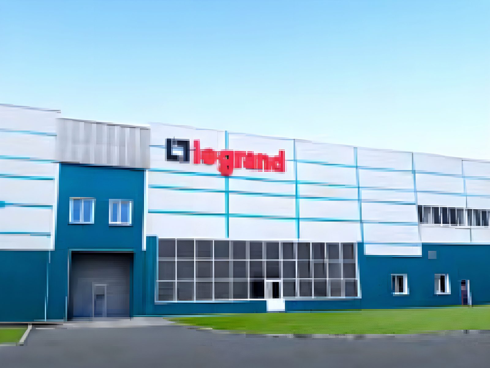 Long white-and-teal panelled facade of the Legrand plant under a clear sky with the red legrand sign on the upper wall