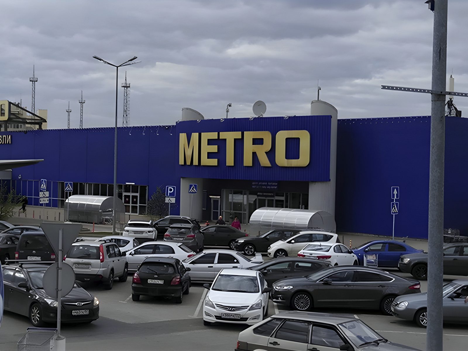 METRO store frontage: blue profiled cladding with the gold METRO sign above a full car park