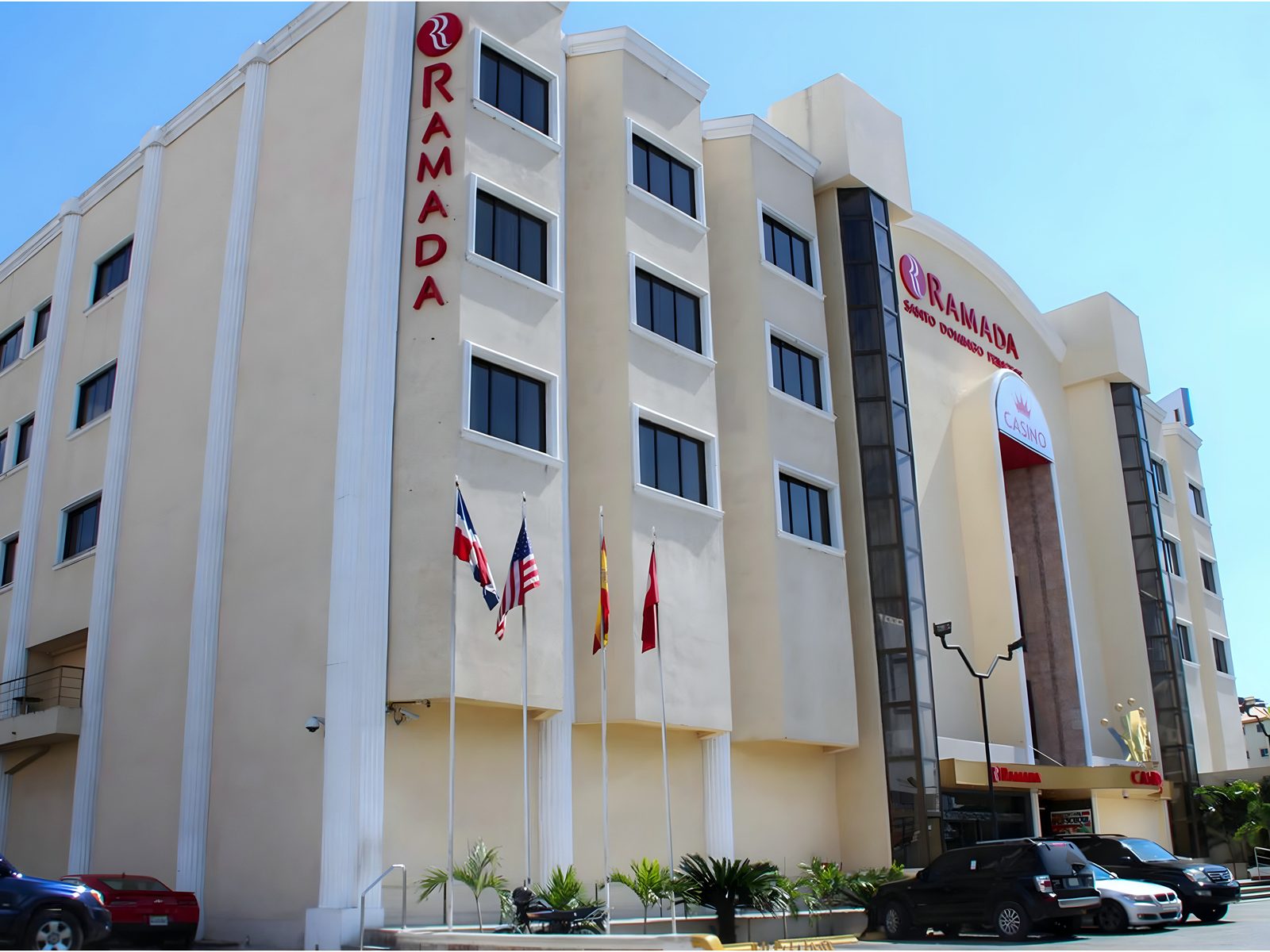 Street-corner view of the Ramada hotel and casino: cream facade, a red RAMADA sign, a CASINO sign over the arched entrance and four flagpoles