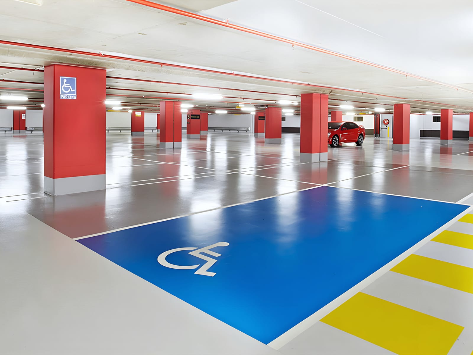Epoxy-floored structural concrete parking deck in Hialeah with red columns, a blue accessible bay and yellow bollards