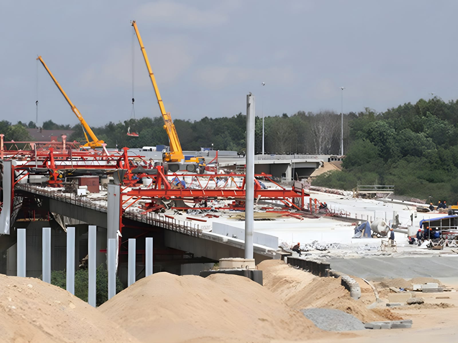 Bridge deck under construction, red formwork trusses and two cranes
