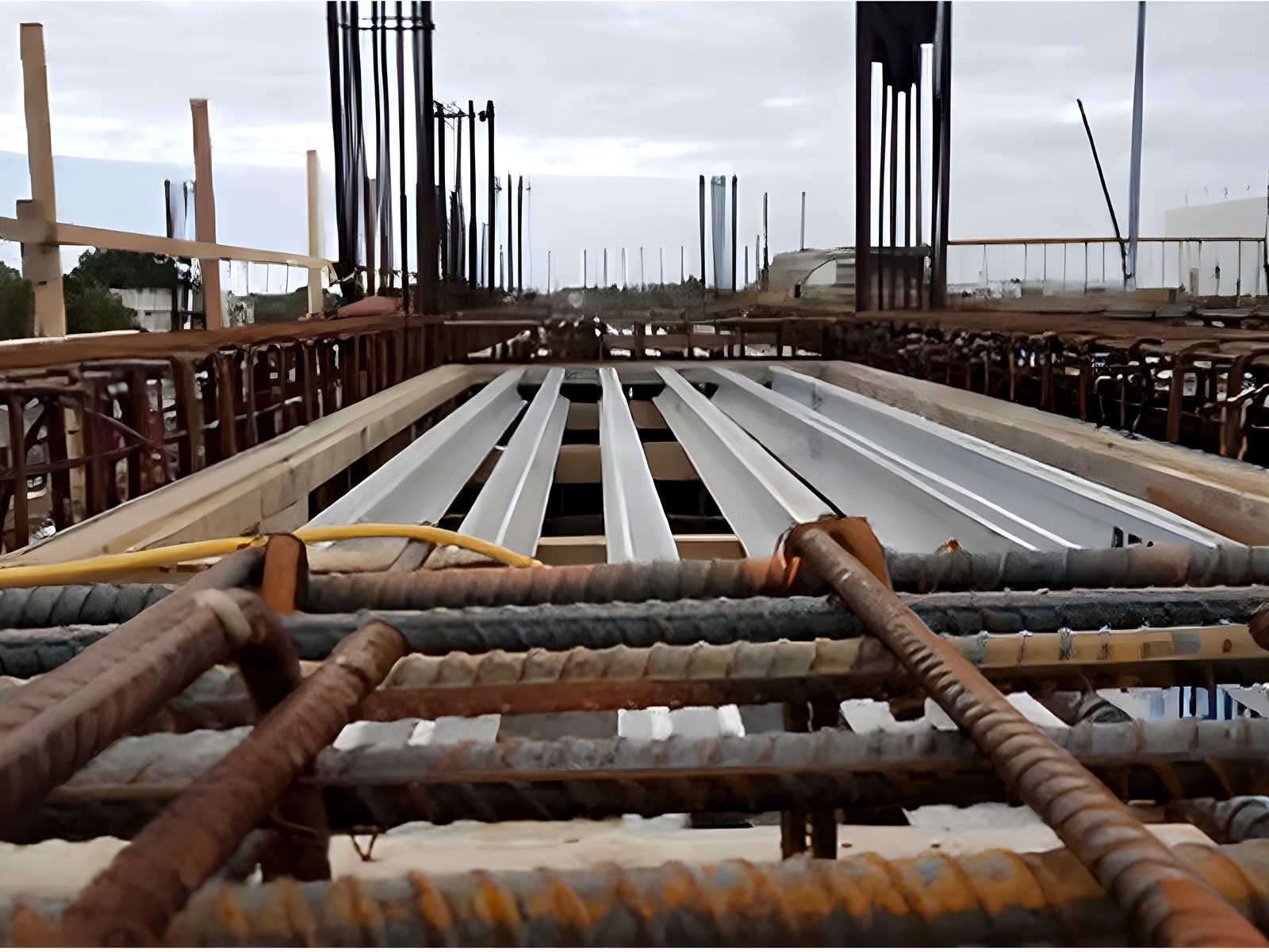 Suspended slab under construction: composite steel deck forms, rebar cages and column starter bars under an overcast sky